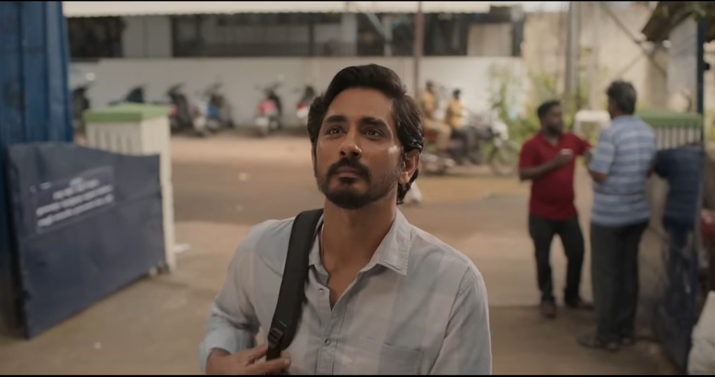 A man dressed in a light-colored shirt carries a shoulder bag as he looks up, with people and parked motorcycles in the background.