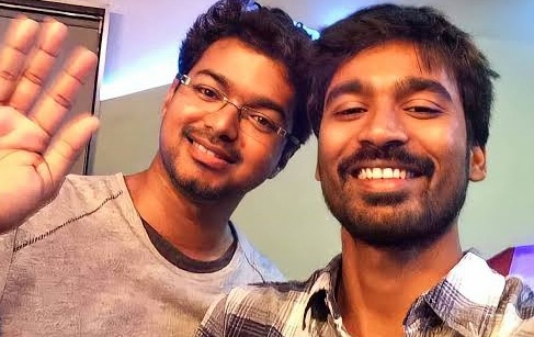 Two young men smiling and posing for a selfie, one waving while the other showcases a broad grin, set against a softly lit background.